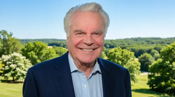 Smiling elderly businessman wearing a navy blue blazer standing outdoors with a scenic green landscape in the background.