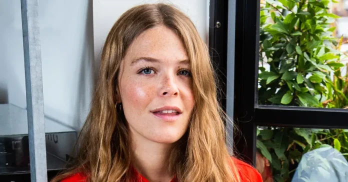 Maggie Rogers Net Worth Maggie Rogers performing on stage, singing passionately with a microphone, spotlight highlighting her as a celebrated singer-songwriter.