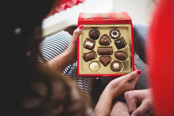 A woman holding a red box of custom chocolates with heart-shaped and assorted designs, making it a perfect gift for any celebration.