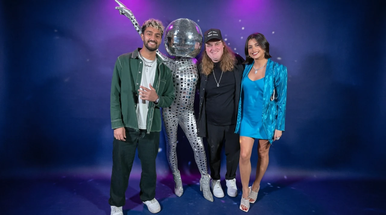 Three people posing beside a reflective silver mascot at an entertainment event with a purple stage background.