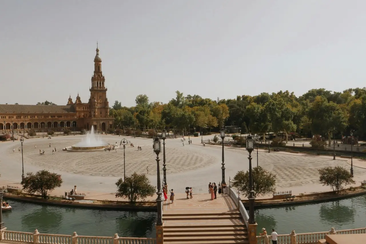 Plaza de España in Seville, Spain featuring the iconic central fountain, historic tower, canal, and pedestrian bridge on a sunny day.