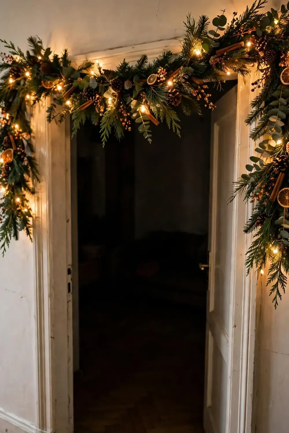 15 Small Apartment Christmas Decor Ideas That Do Not Take Floor Space 2 Christmas garland with warm lights, pinecones, and dried orange slices along the top of a white door frame.